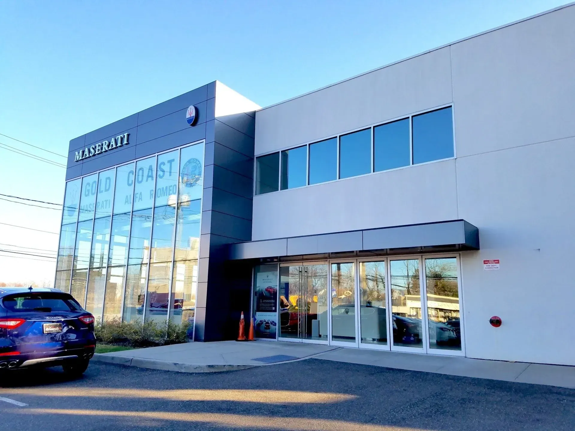 Maserati dealership on the coast with a blue car parked outside, glass windows, and blue sky.