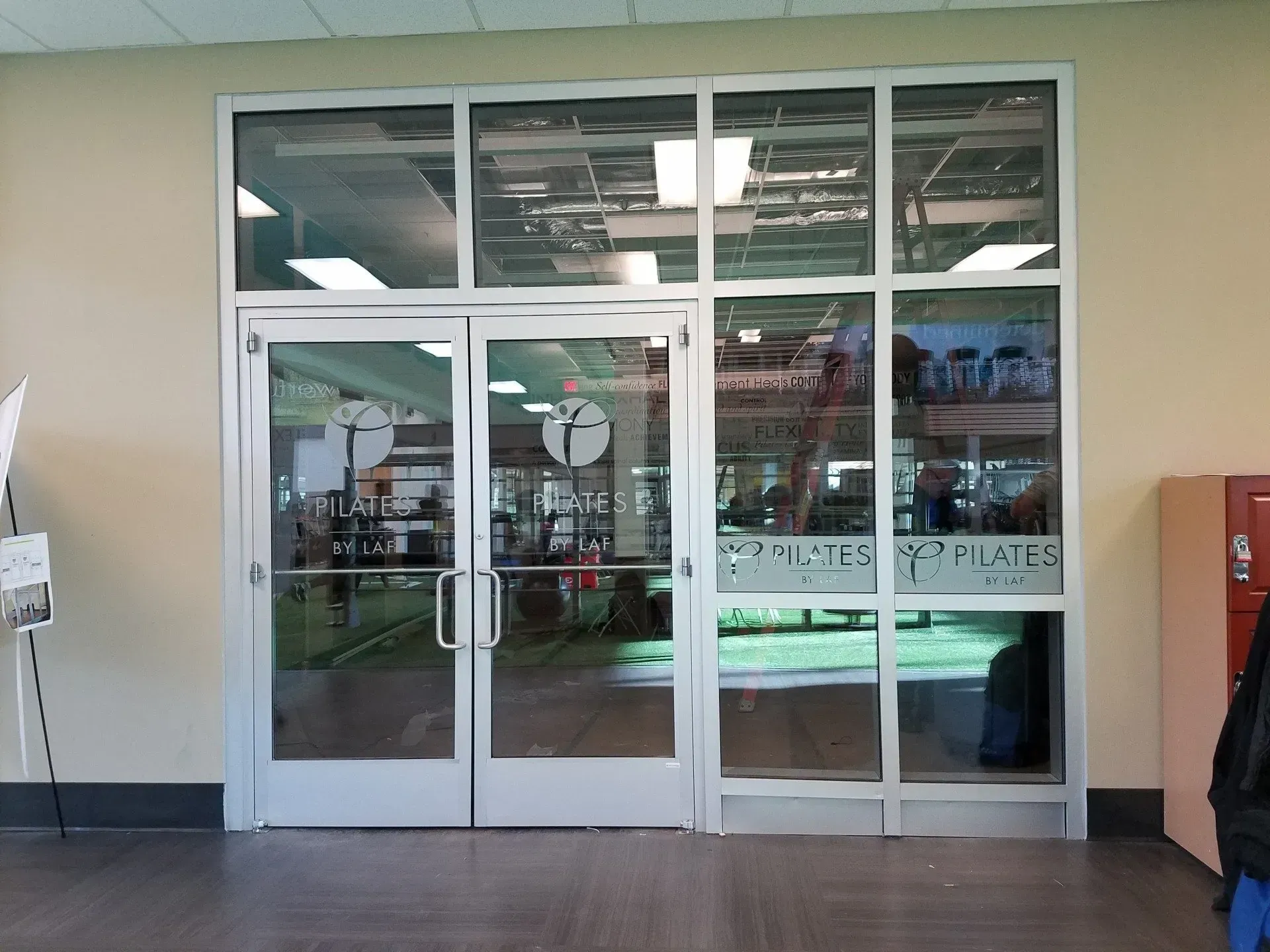 Glass double doors with side windows. White frames, lettering, and a logo. Interior visible.