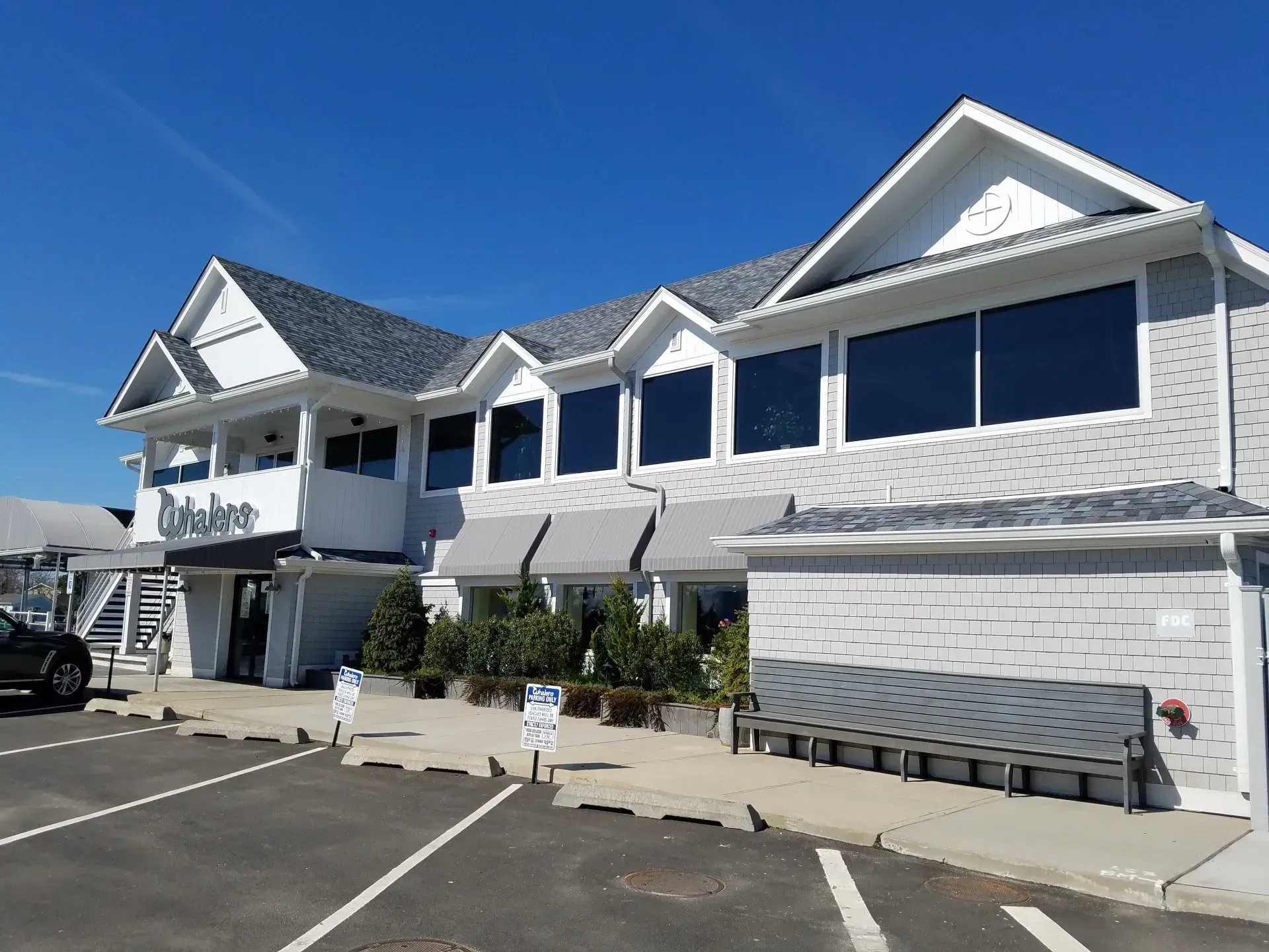 Exterior view of a light gray building, with dark tinted windows, awnings, and a parking lot. 