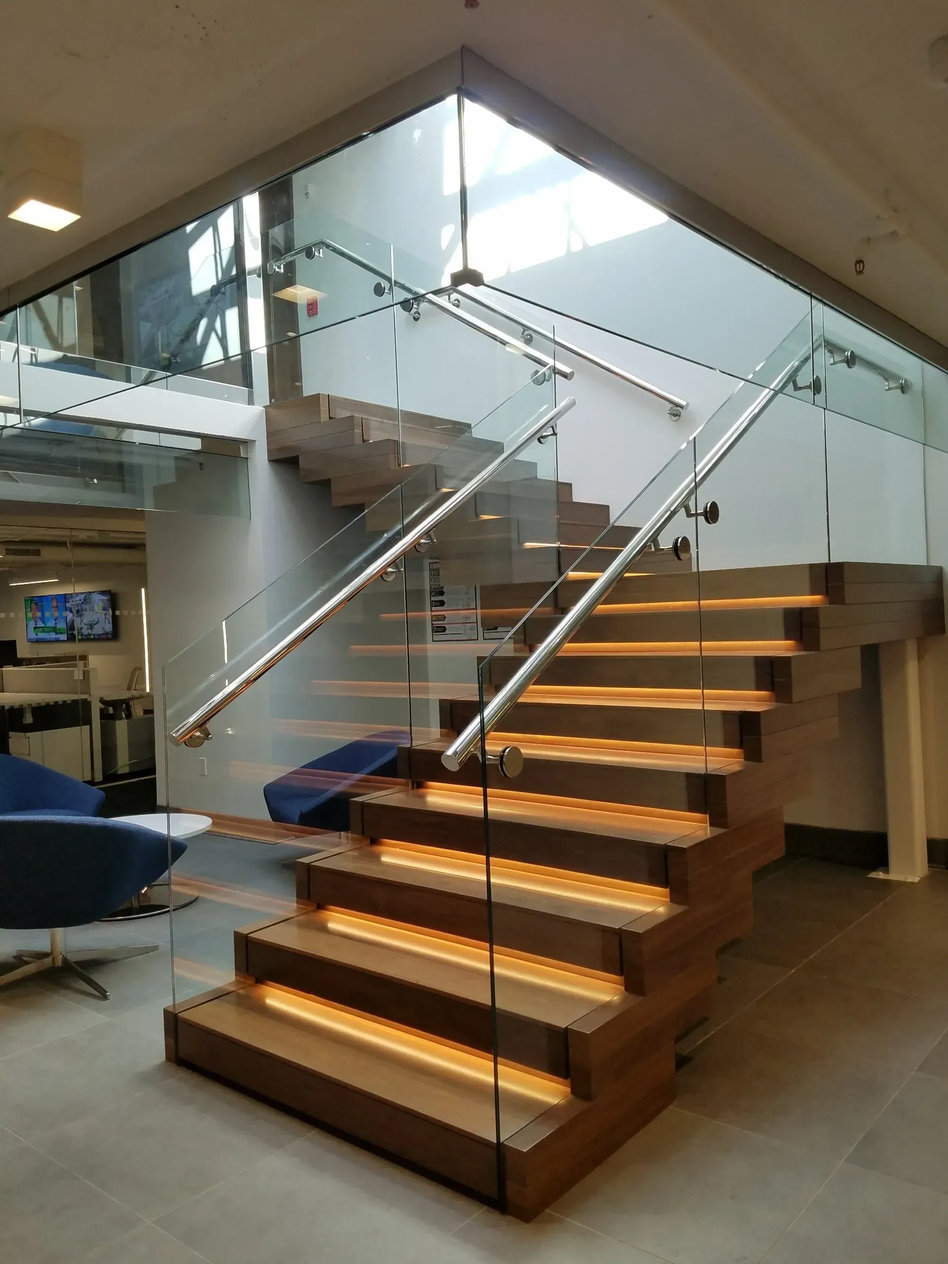 Wooden staircase with glass railing and LED lighting, in a modern office space.
