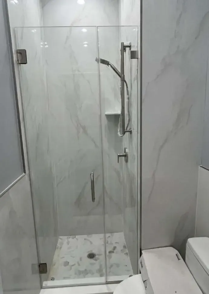 Glass shower enclosure with brushed nickel fixtures in a tiled bathroom.