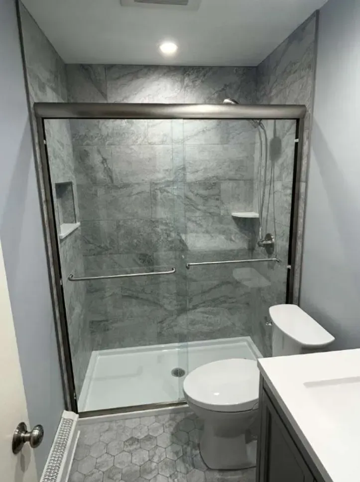 Bathroom with gray tiled shower and glass sliding doors, toilet, and hexagonal floor tiles.