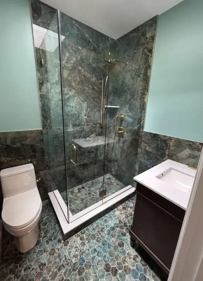 Modern bathroom with teal, gray, and brown stone shower enclosure and floor, a toilet, and vanity.