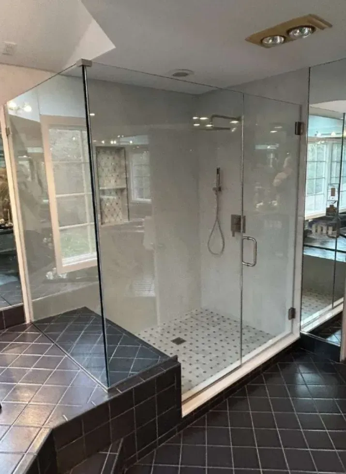 A modern glass shower with white and black tiled floors, in a bathroom.