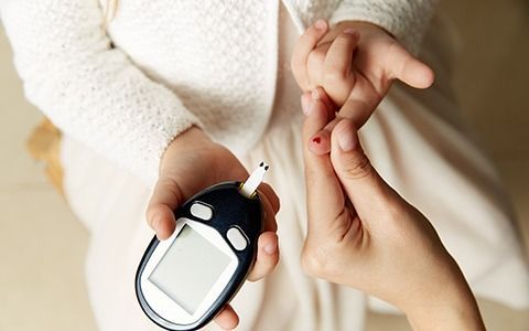 Person testing blood sugar with a glucose meter on a child's finger. White clothing, indoor setting.