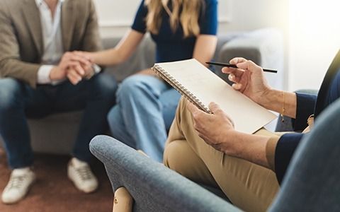 Therapist taking notes during a couple's therapy session; hands clasped, light setting.