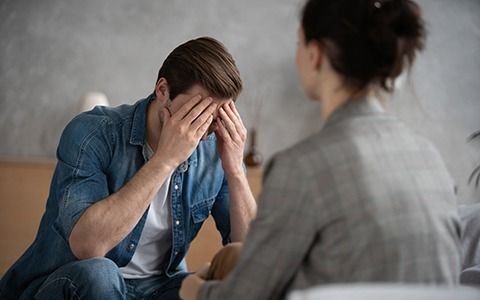 Man in distress, hands on face, seated in front of therapist.