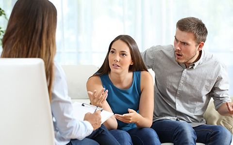A couple arguing during couples therapy. A therapist sits with them, taking notes.