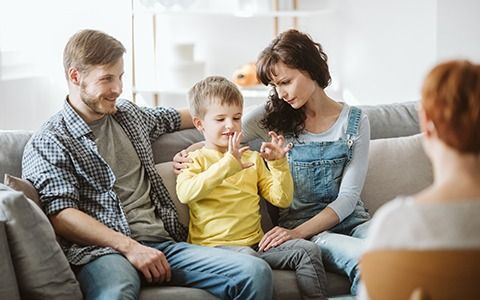 Family on a couch, son signing with hands, parents watching, and a counselor.