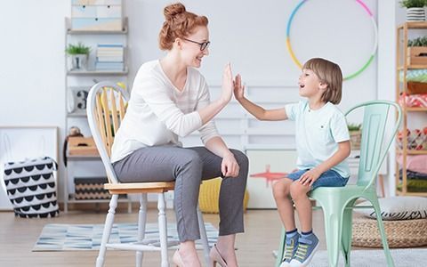 Woman and boy giving a high five, smiling. They sit on chairs indoors.