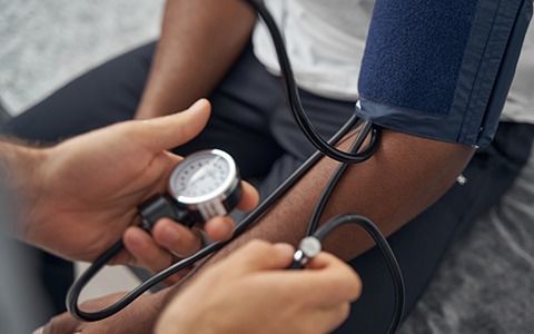 Doctor taking patient's blood pressure with a sphygmomanometer; arm with blue cuff, silver dial.
