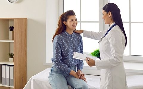 A doctor in a white coat, with a stethoscope, consults with a smiling patient.