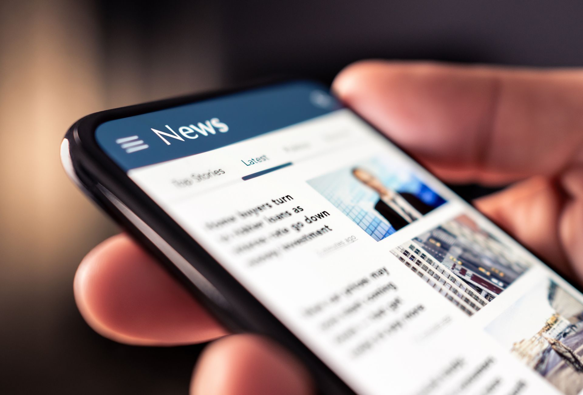 Person holding a smartphone displaying a news app, blue header, headlines visible.