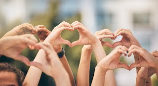 Hands forming heart shapes against a blurred outdoor background.