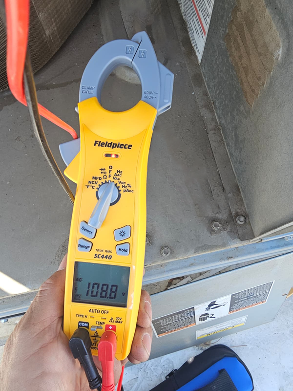 Yellow digital clamp meter measuring a cable in a utility box, display reading 10.88