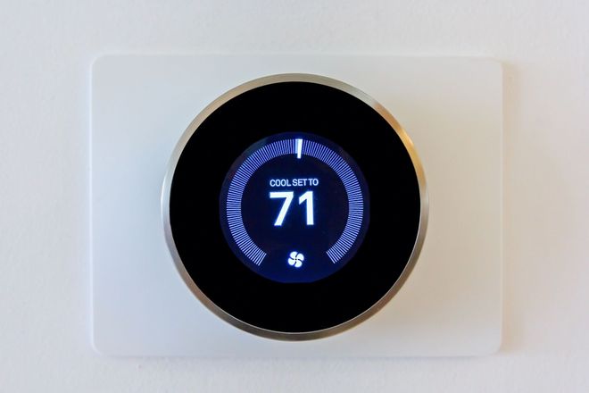 Smart thermostat on a white wall displaying 71° with a blue circular interface