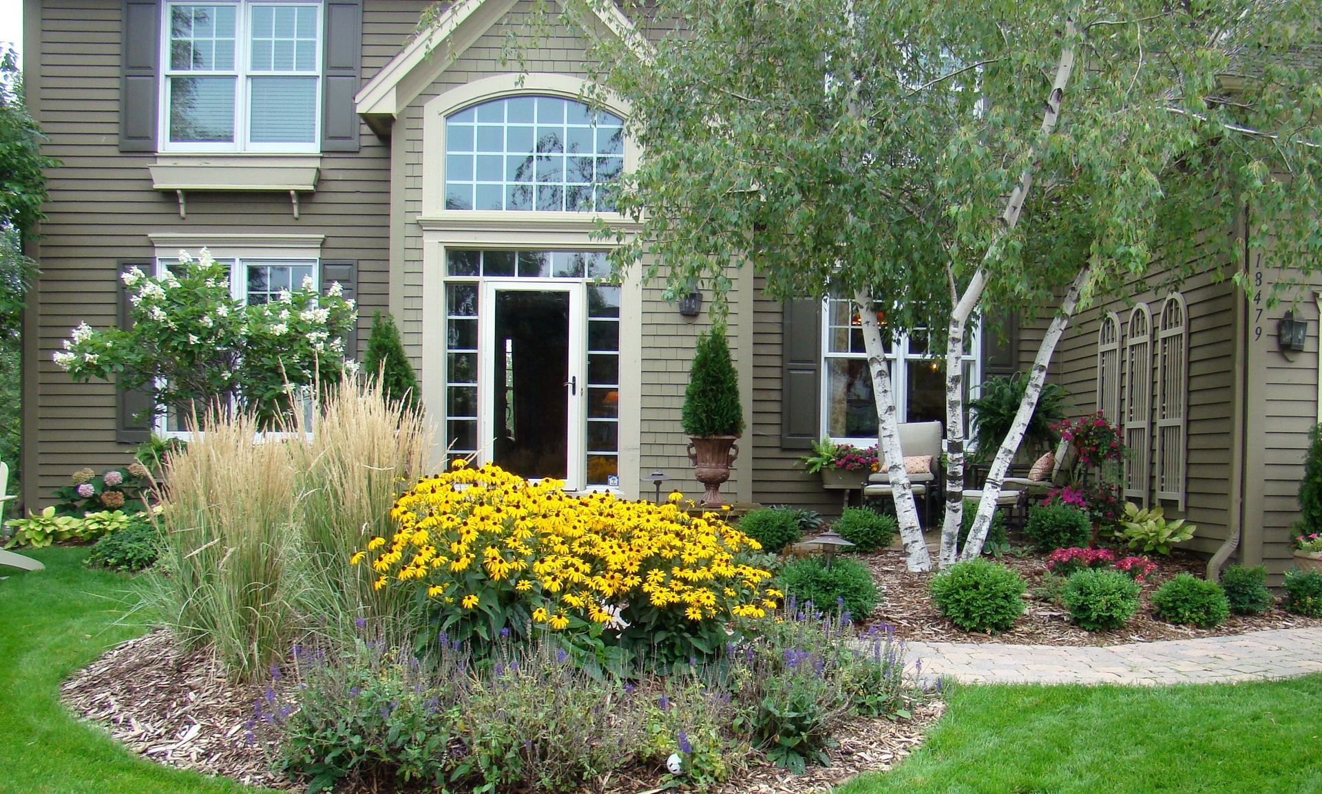 House with landscaped front yard; yellow flowers, birch tree, green lawn.