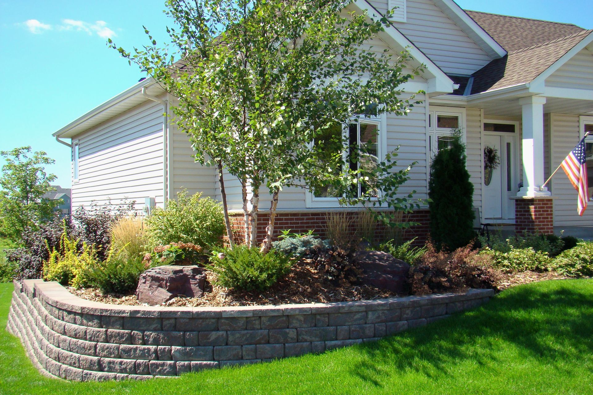 Landscaped yard with a retaining wall in front of a house.