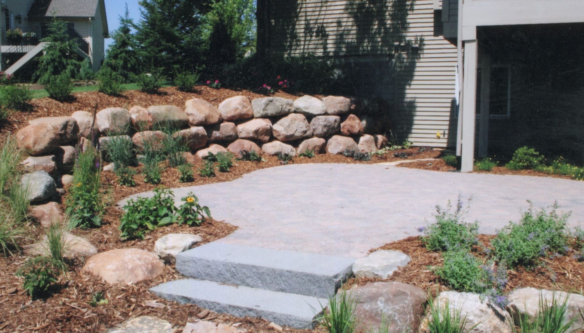 Patio with stone steps, a rock wall, and landscaping.
