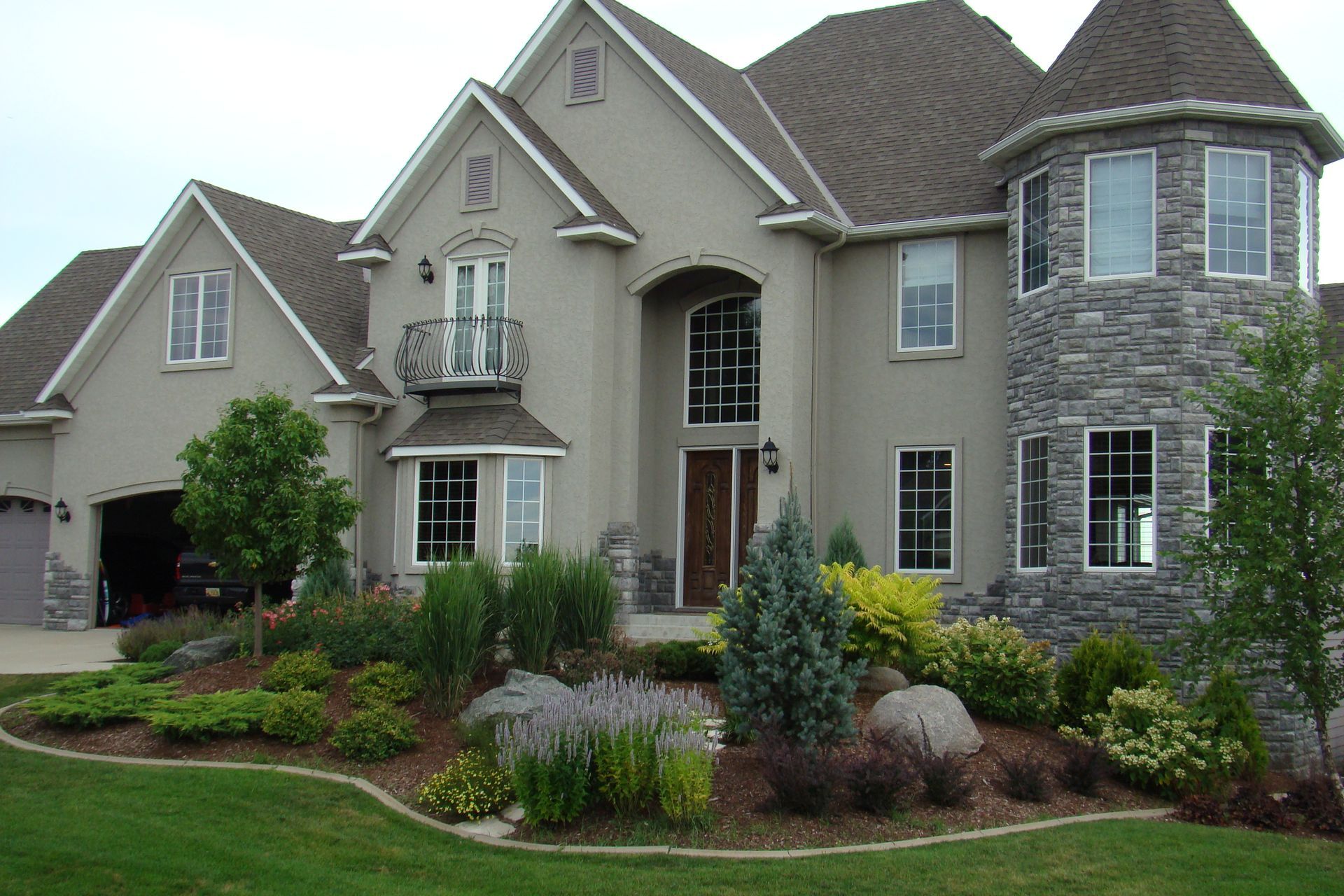 Large gray stucco house with stone tower and landscaped front yard.