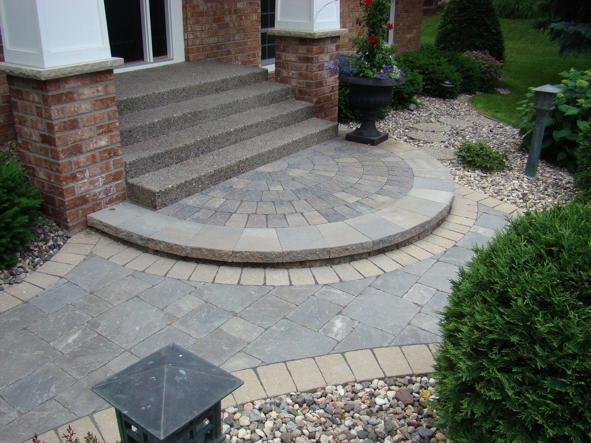 Brick steps and paved entryway leading to a home with landscaping and a decorative planter.