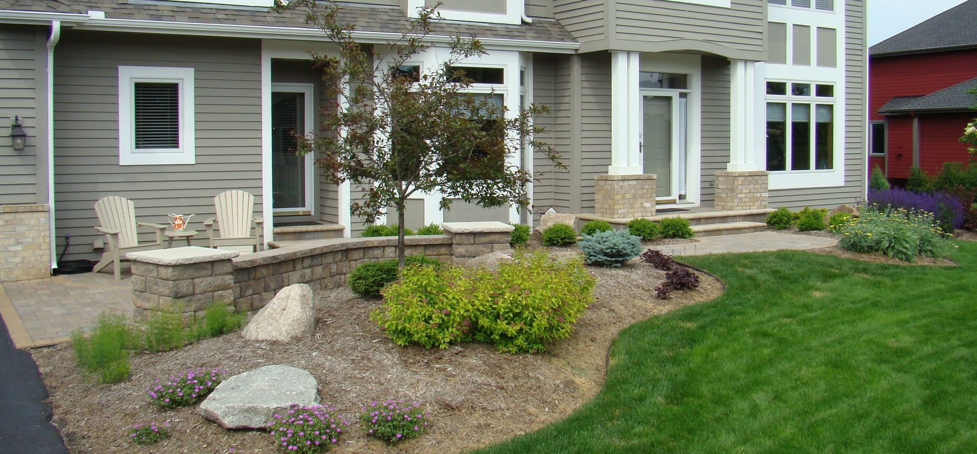 Landscaped yard with stone edging, lawn, and house with gray siding and white trim.