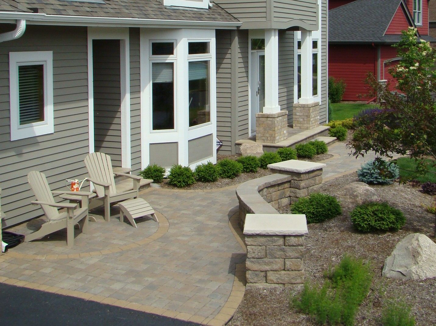 Patio with stone pavers, two chairs, and landscaping in front of a house.