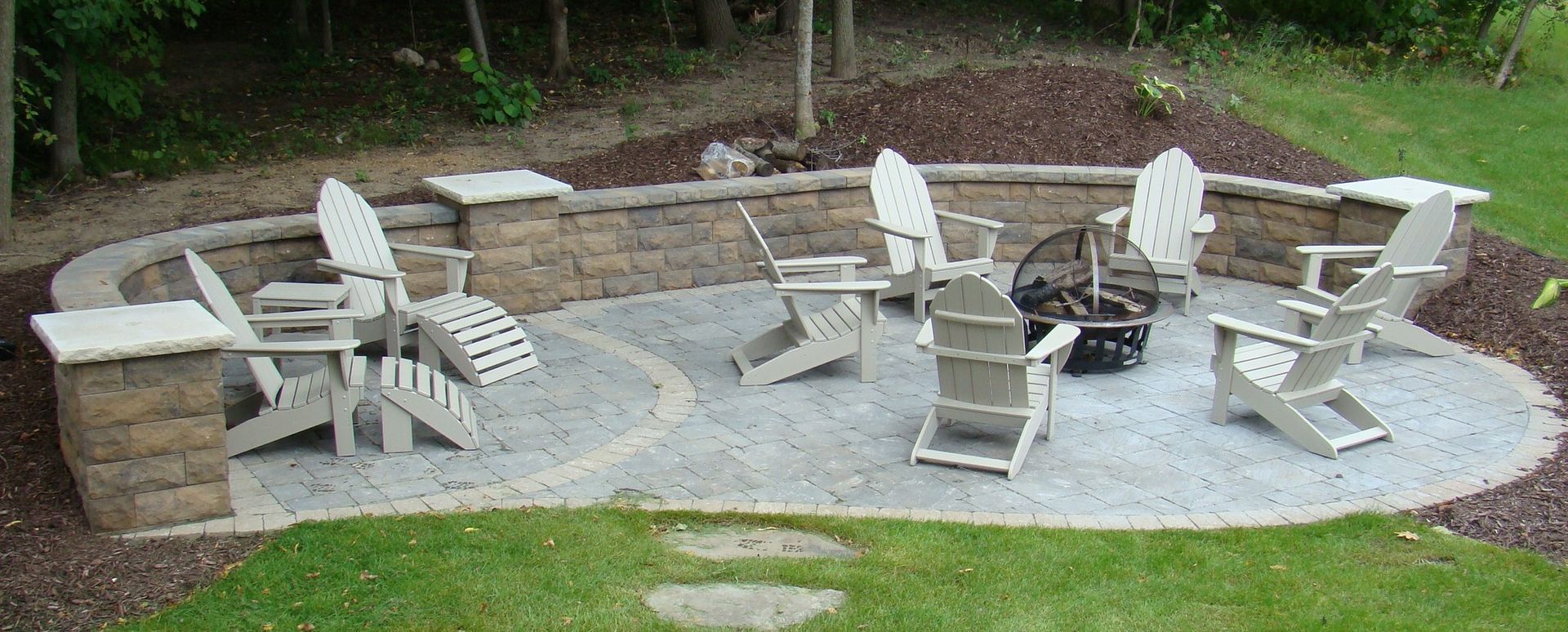 Outdoor patio with Adirondack chairs surrounding a fire pit, bordered by a stone wall.