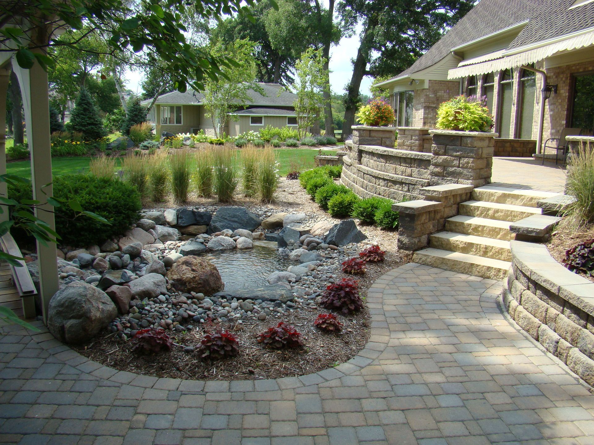 Landscaped backyard with a pond, stone patio, steps, and house.