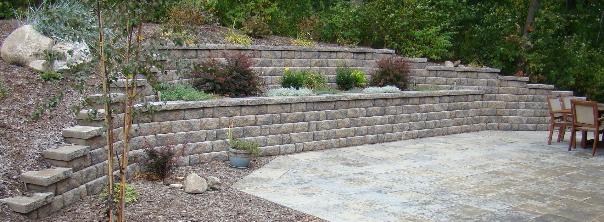 Stone retaining wall with plants and a stone patio.
