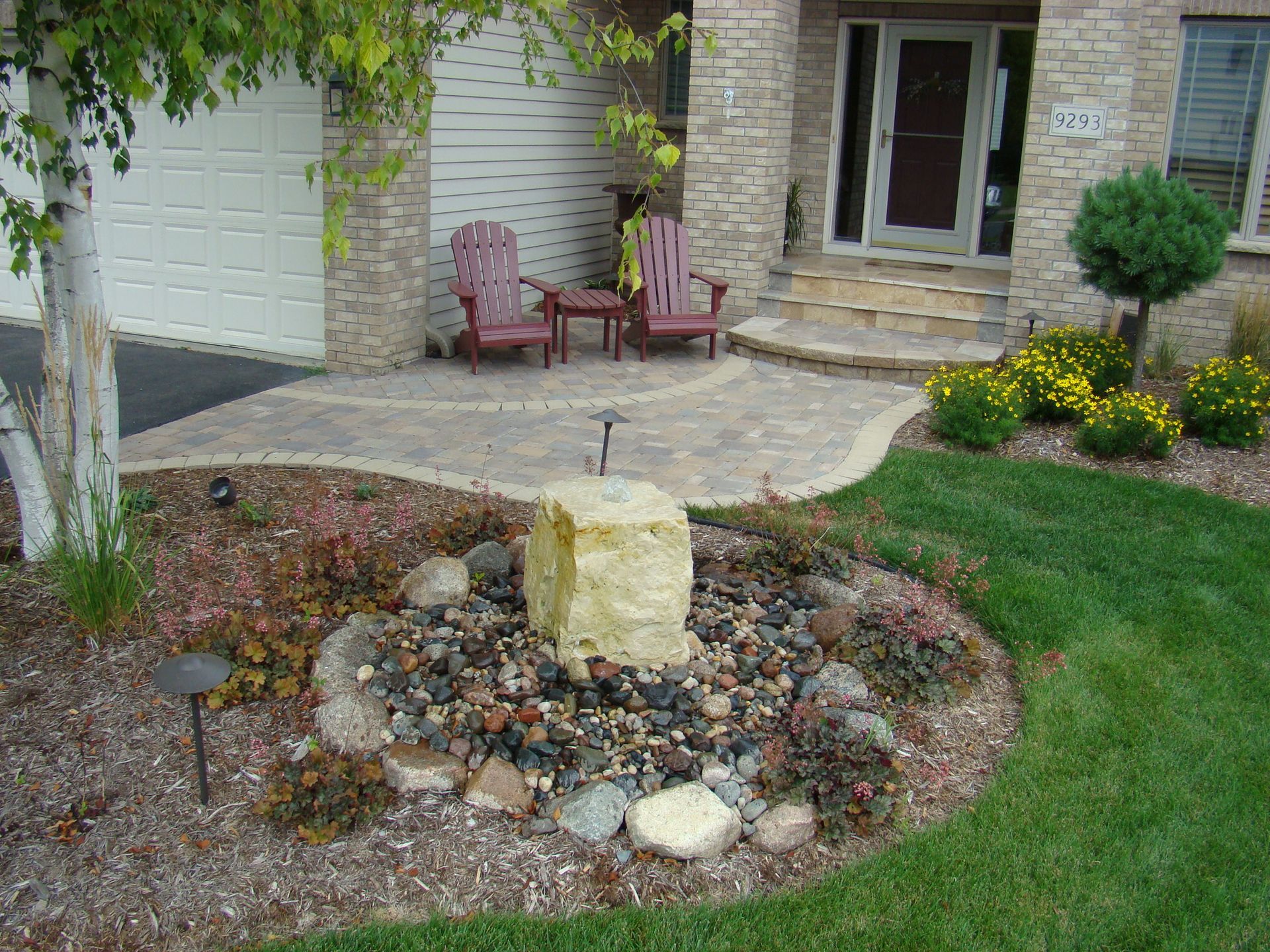 Front yard landscaping with stone walkway, fountain, and flower beds.
