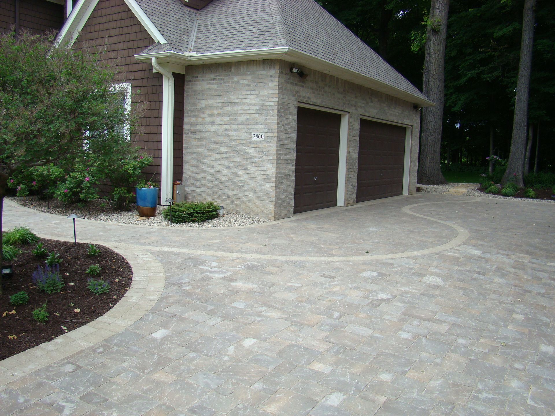 Brick garage with brown doors, connected to house, with paved driveway and landscaping.