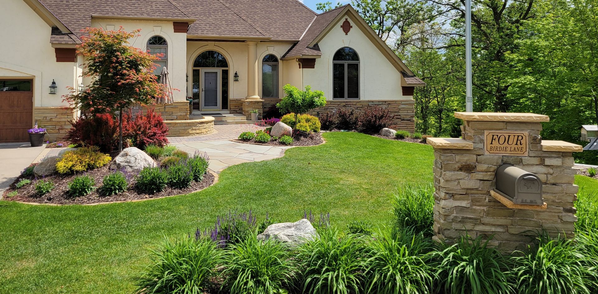 A house with lush green lawn, landscaped front yard, stone mailbox, and a red tree.