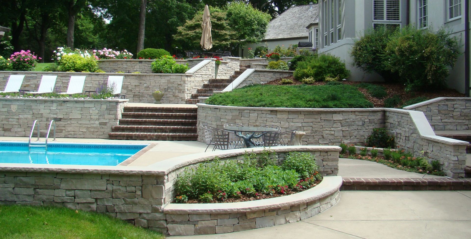 Stone terraced backyard with pool, patio, and lush landscaping.