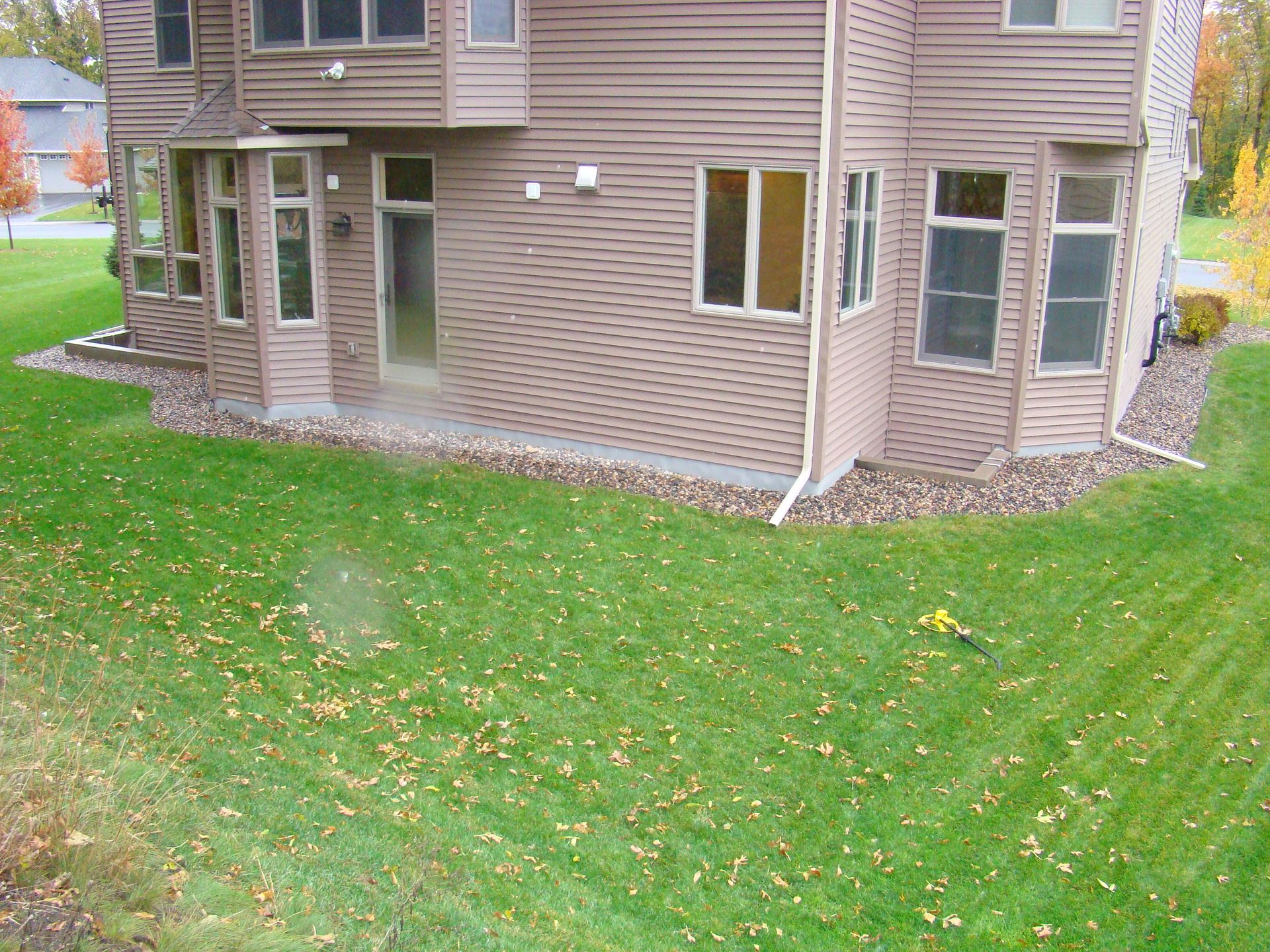 Brown house with green lawn, windows, and a small garden bed along the foundation.