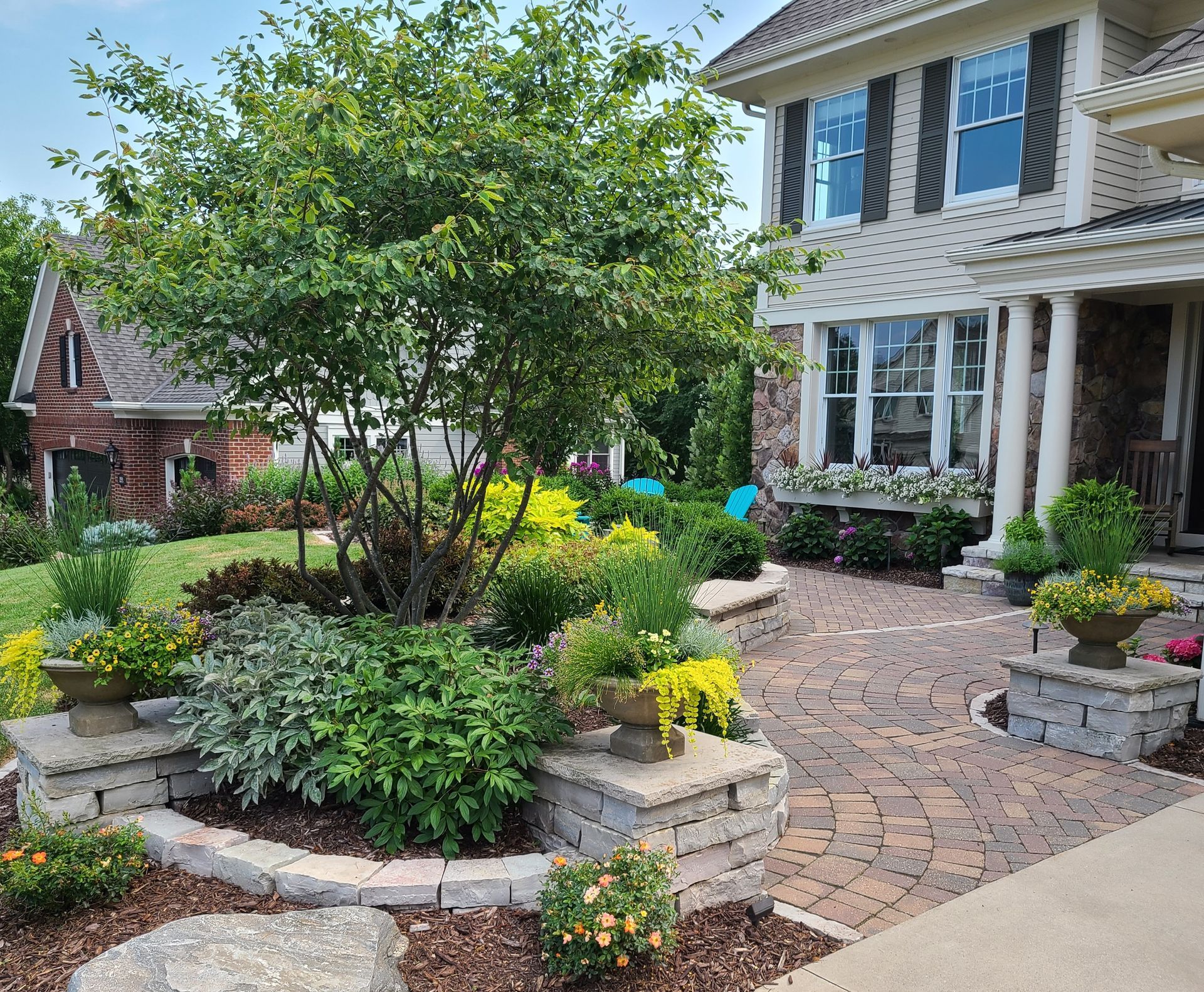 Landscaped front yard with brick walkway, stone retaining walls, and flowering shrubs in front of a house.
