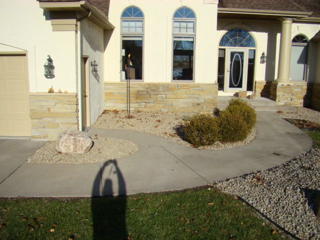 Concrete walkway leading to a house with beige walls and a green lawn.
