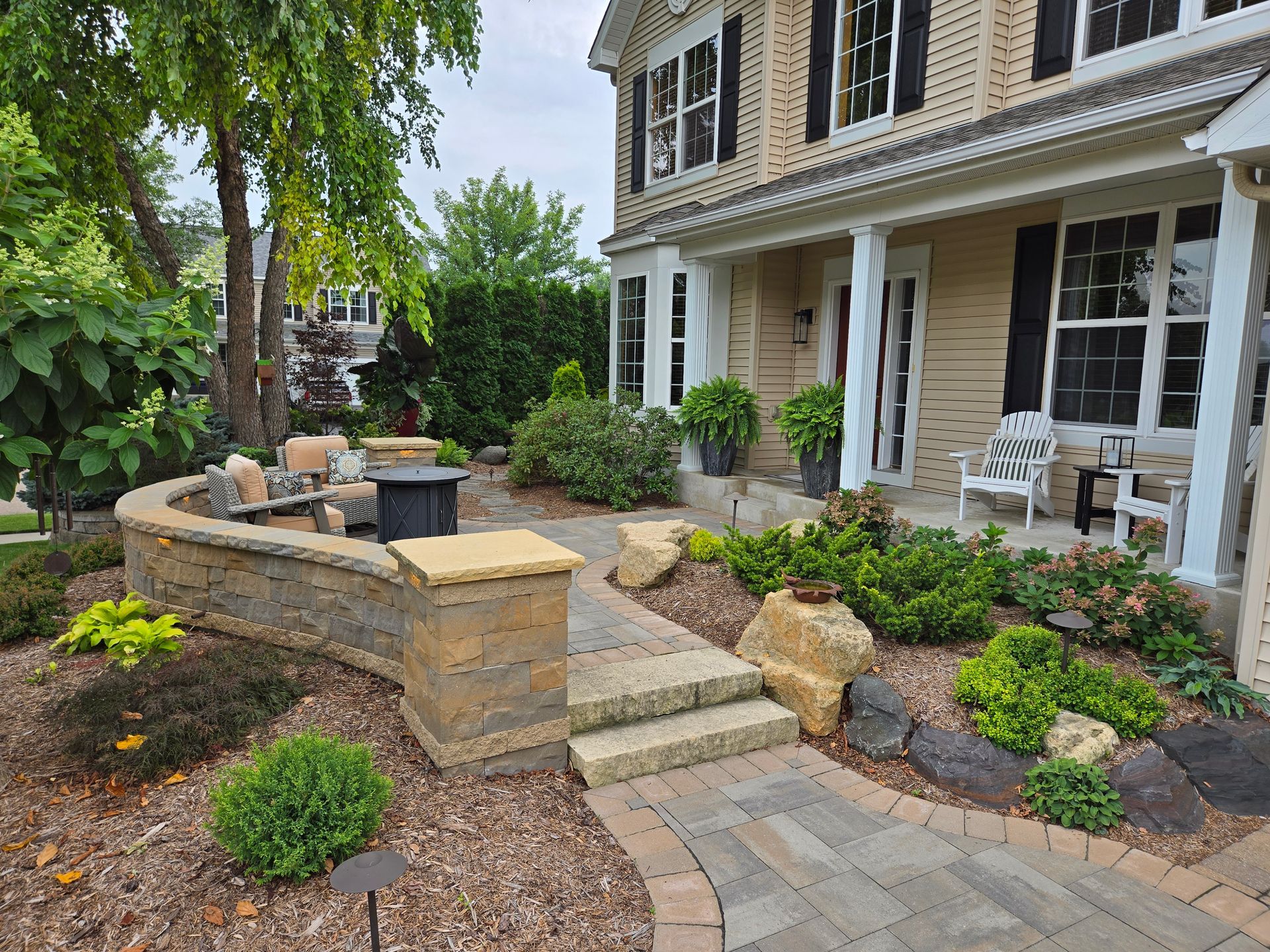 Stone pathway leading to a two-story home with a porch, surrounded by landscaped gardens and a retaining wall.