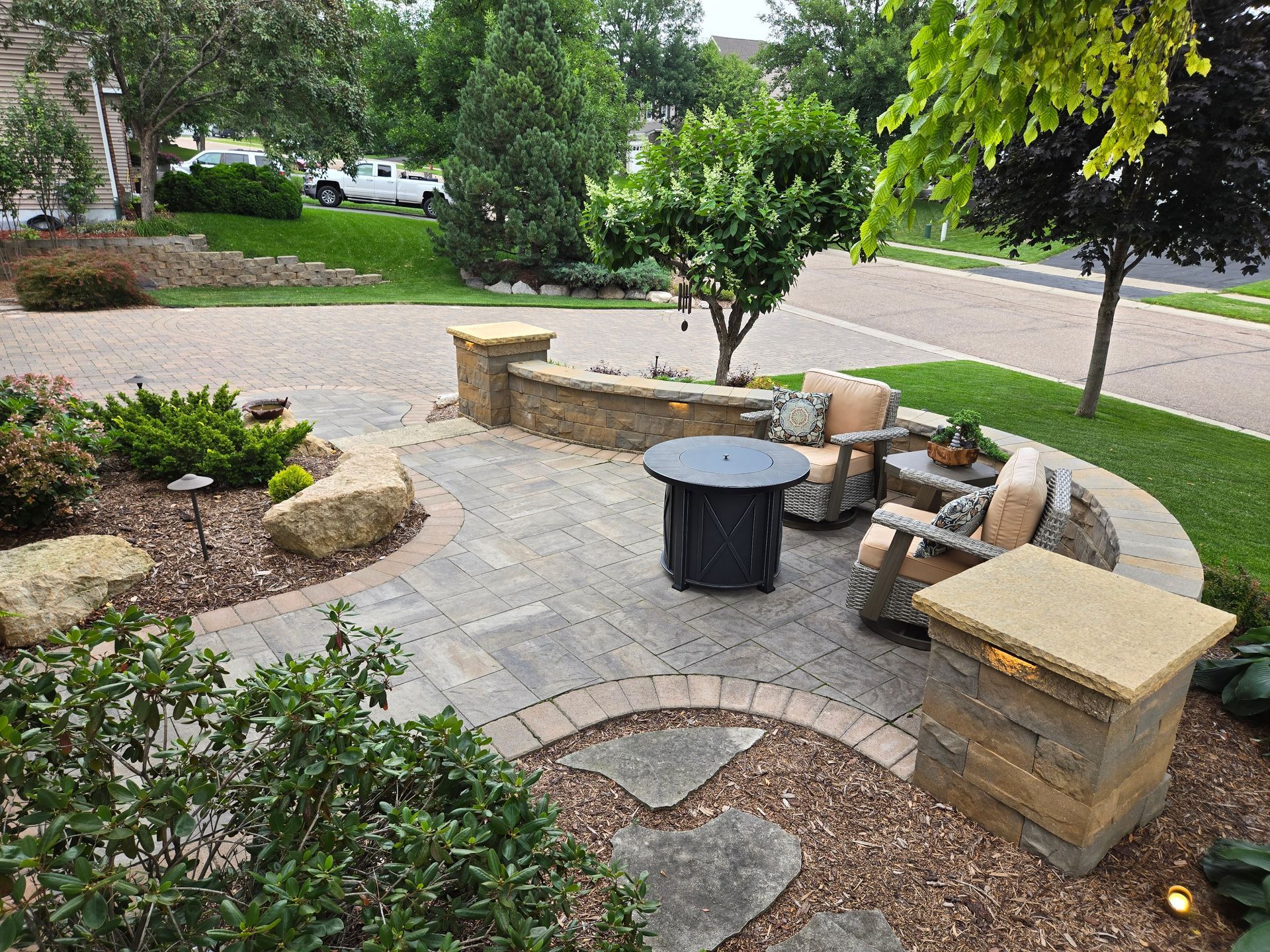 Stone patio with fire pit, seating, and landscaping.