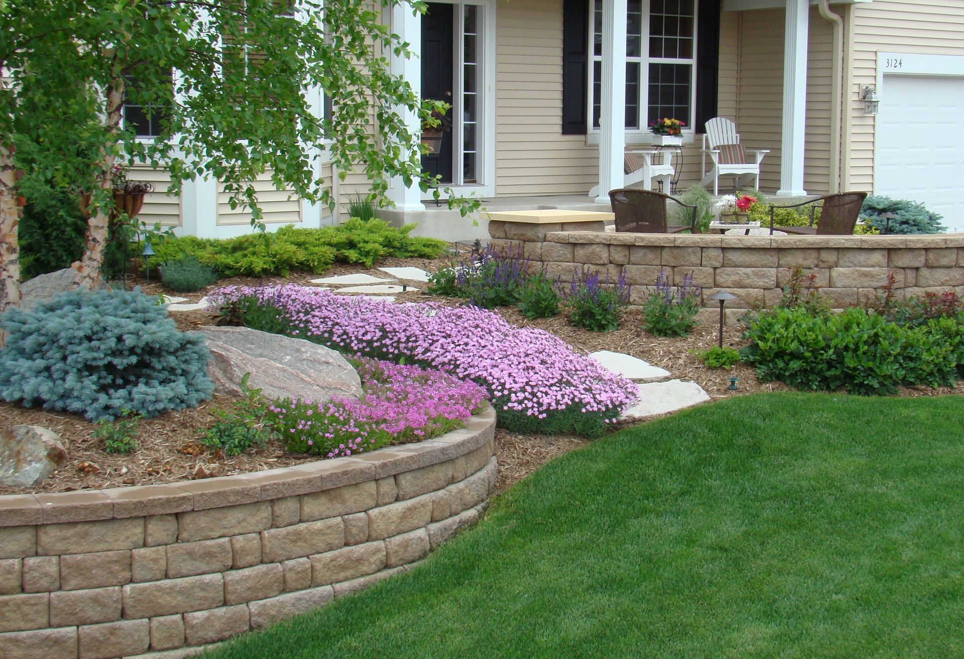 Landscaped front yard with brick retaining walls, blooming purple flowers, and green lawn.