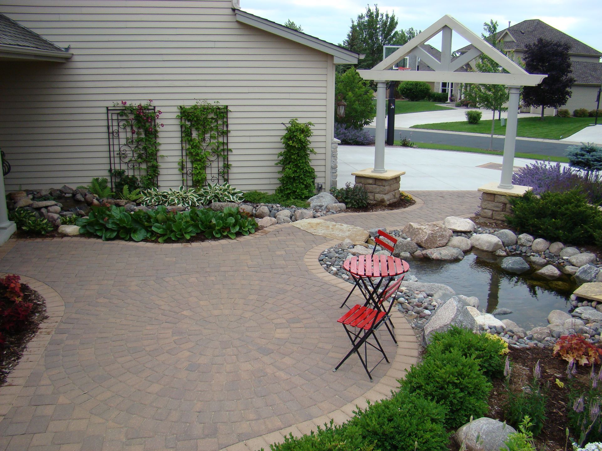 Patio with a small table and chairs, a pond, and a trellis. The setting appears to be a house exterior.