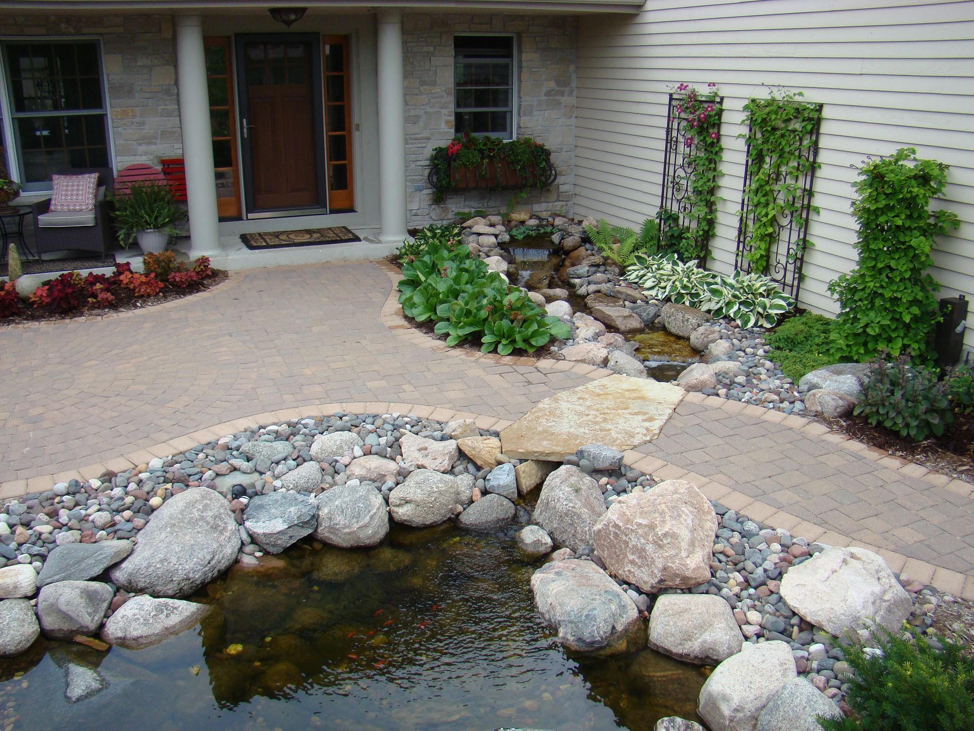 A home's entrance with a decorative pond, waterfall, stone path, and vibrant landscaping.