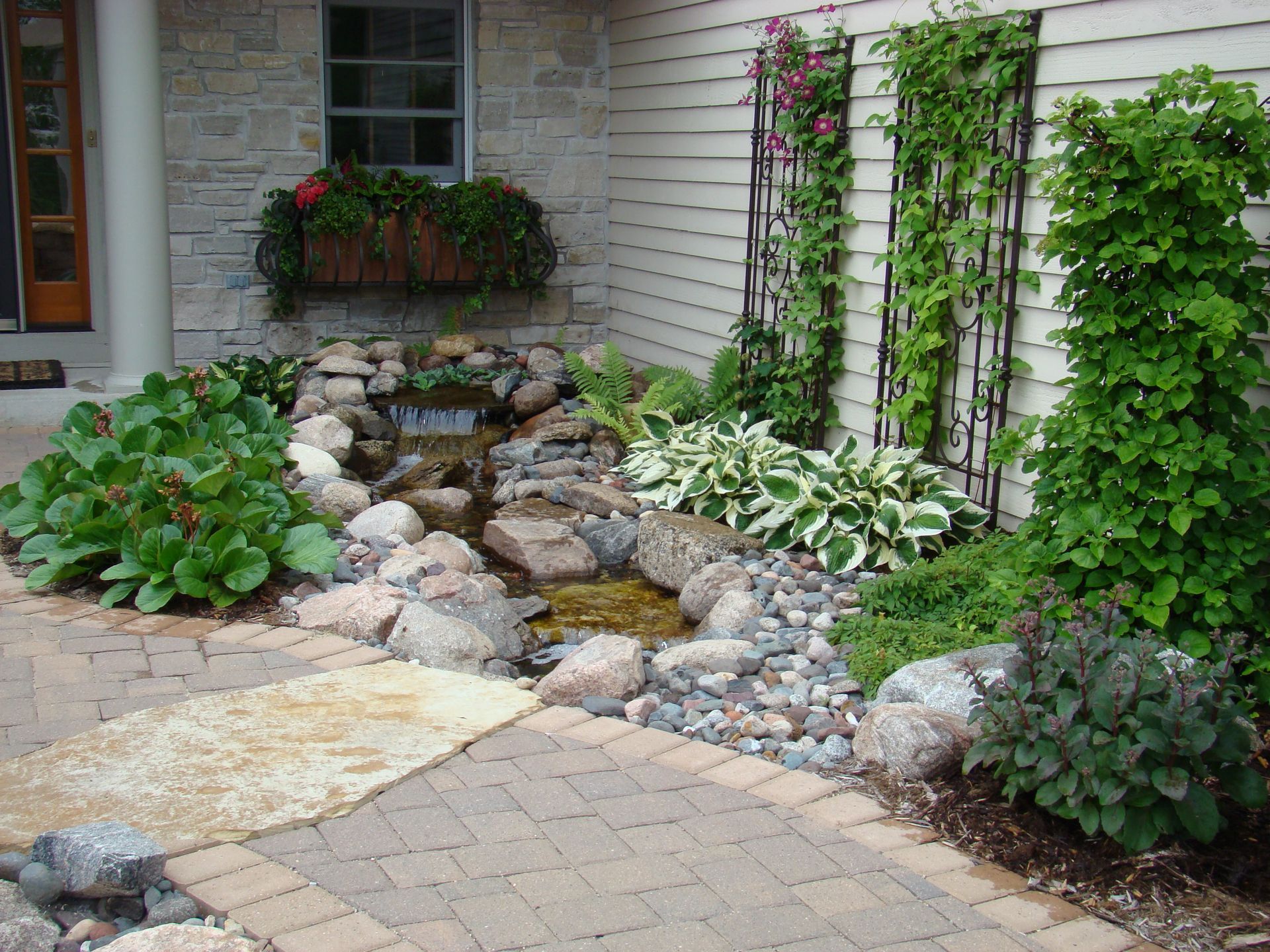 Water feature with stream and lush landscaping by a brick patio.