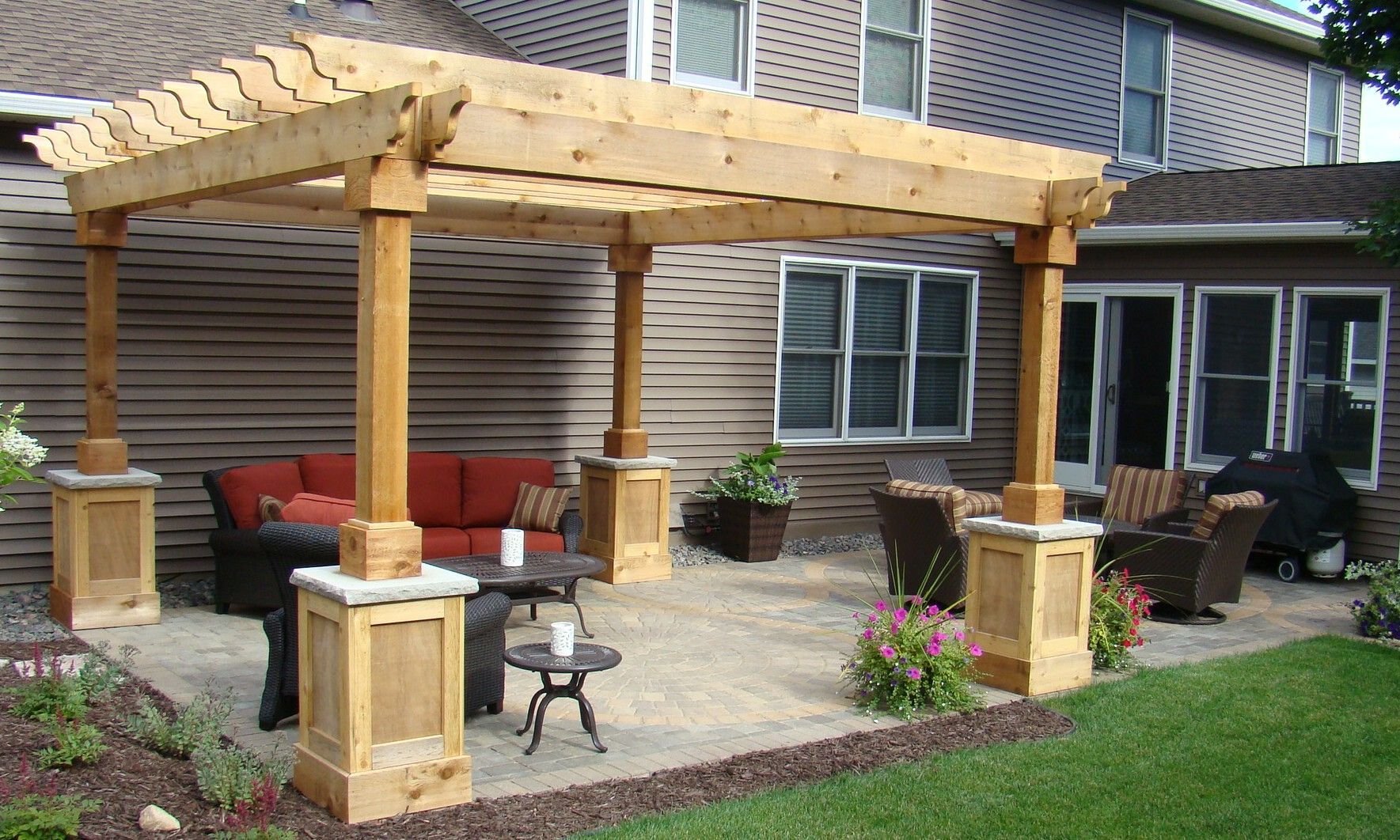 Wooden pergola over patio with seating, gravel, and grass.