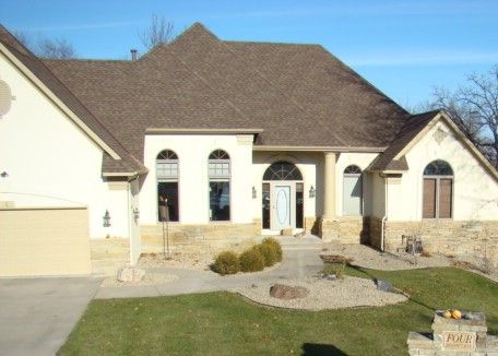 Beige house with a brown roof and arched windows; stone accents.