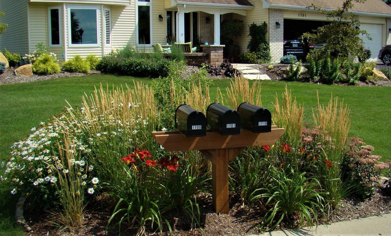 Mailboxes in a flower bed in front of a yellow house with green lawn.