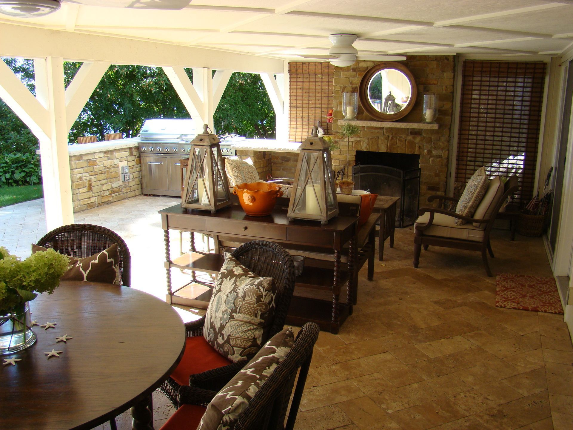 Covered outdoor patio with seating, fireplace, and grill.
