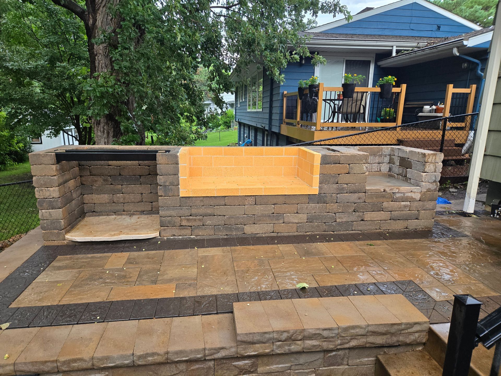 Stone patio with a partially built brick outdoor kitchen and raised seating area.