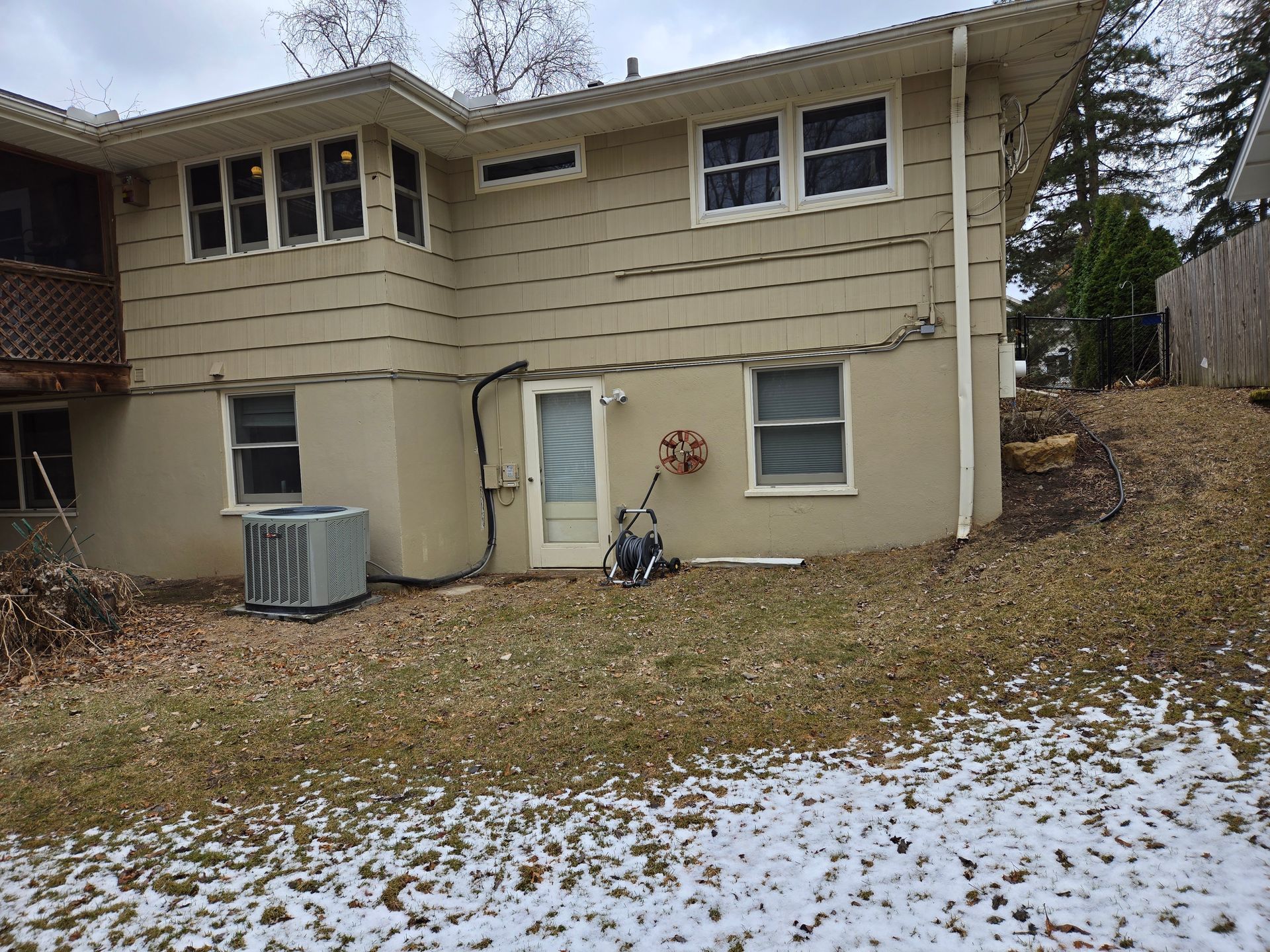 Beige house exterior with windows, door, AC unit, and snowy yard.