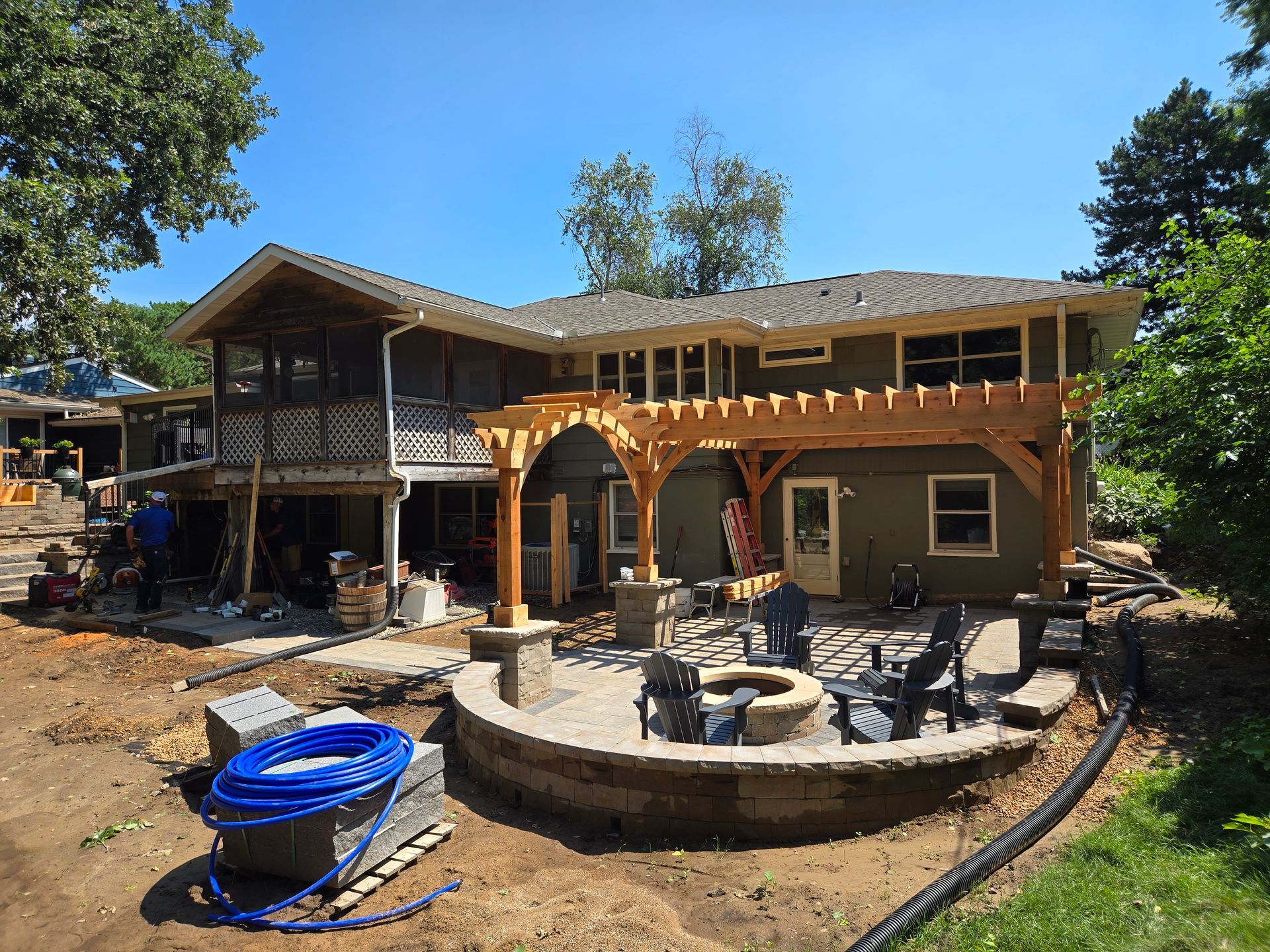 Backyard with newly built deck, pergola, and fire pit under construction on a sunny day.